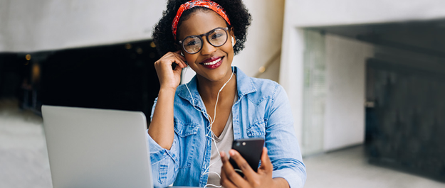 A happy young woman student sitting at home with her laptop, phone and headphones smiling at the camera. smaller version of report cover for Majoring in Money 2019